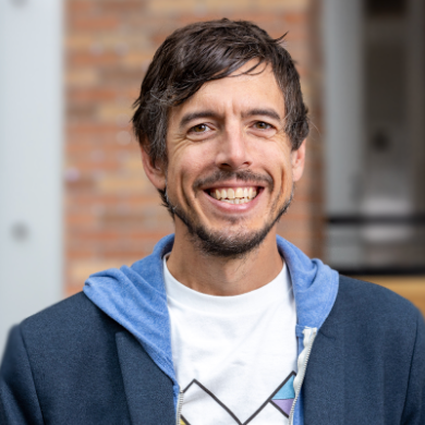 Headshot of Jon Froehlich, a white man with brown hair. He is wearing a t-shirt, hoodie, and a suit coat and is smiling effusively.